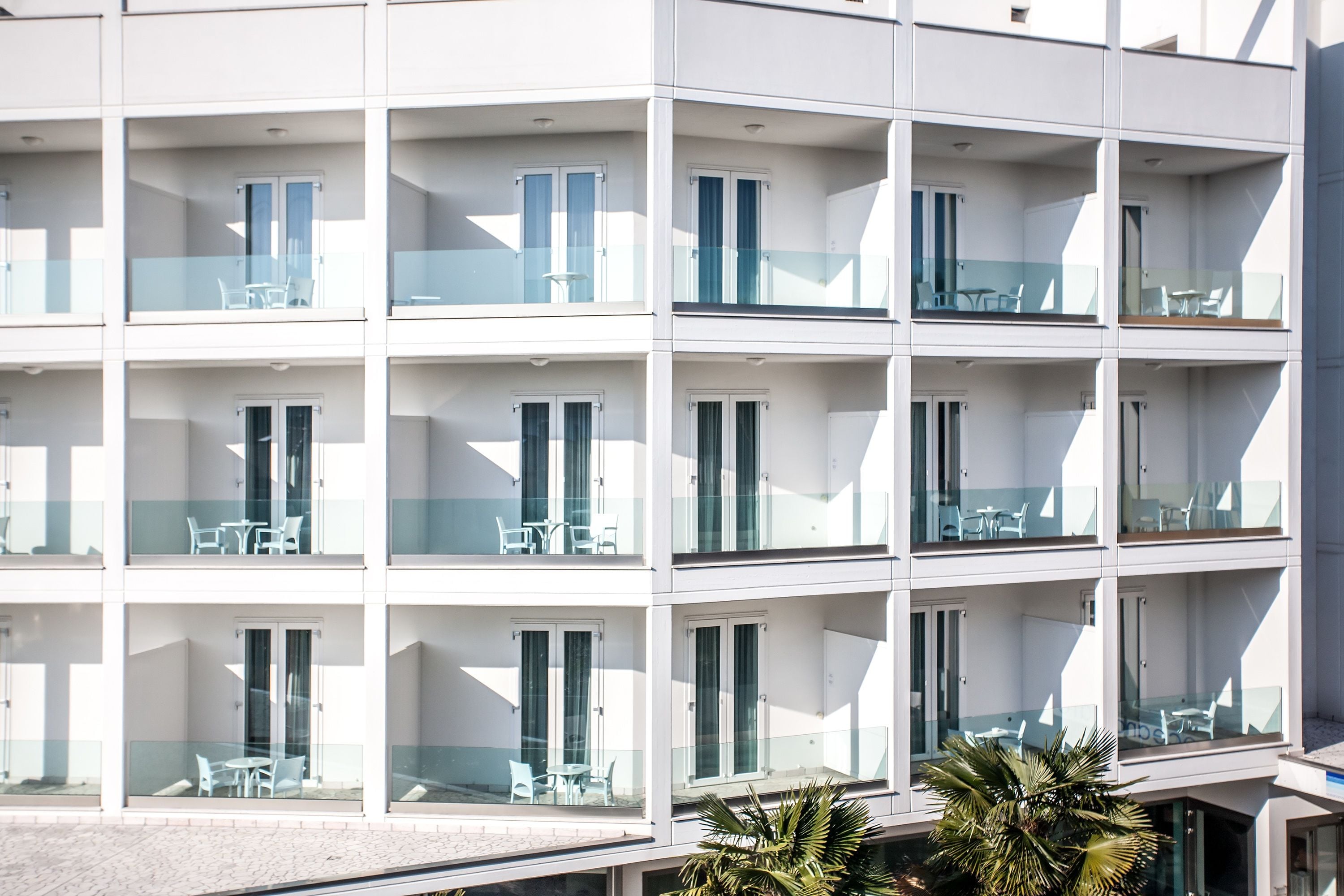 A multi-story hotel with balconies, each featuring glass railings and outdoor seating.