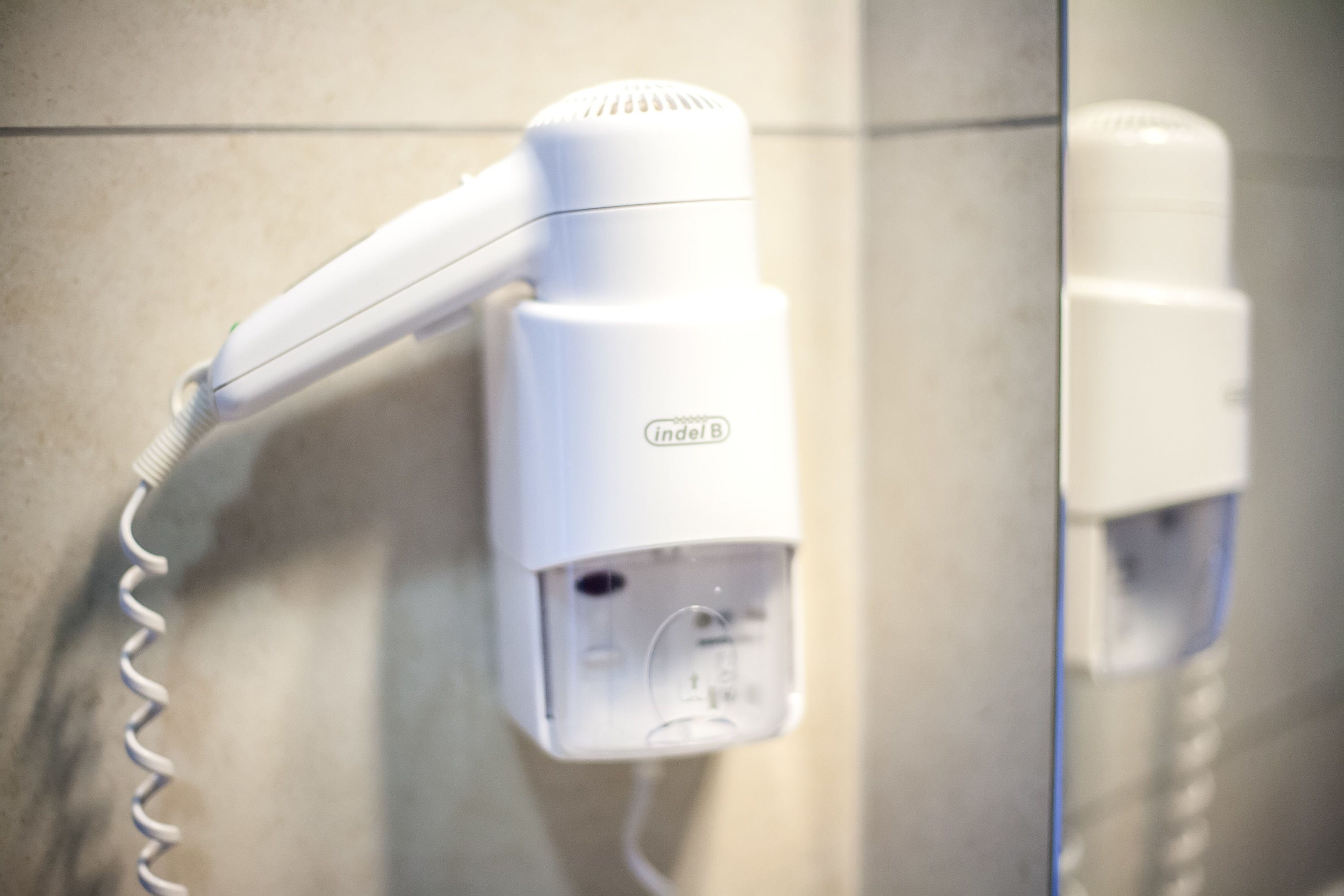 A white hair dryer mounted on a tiled wall.