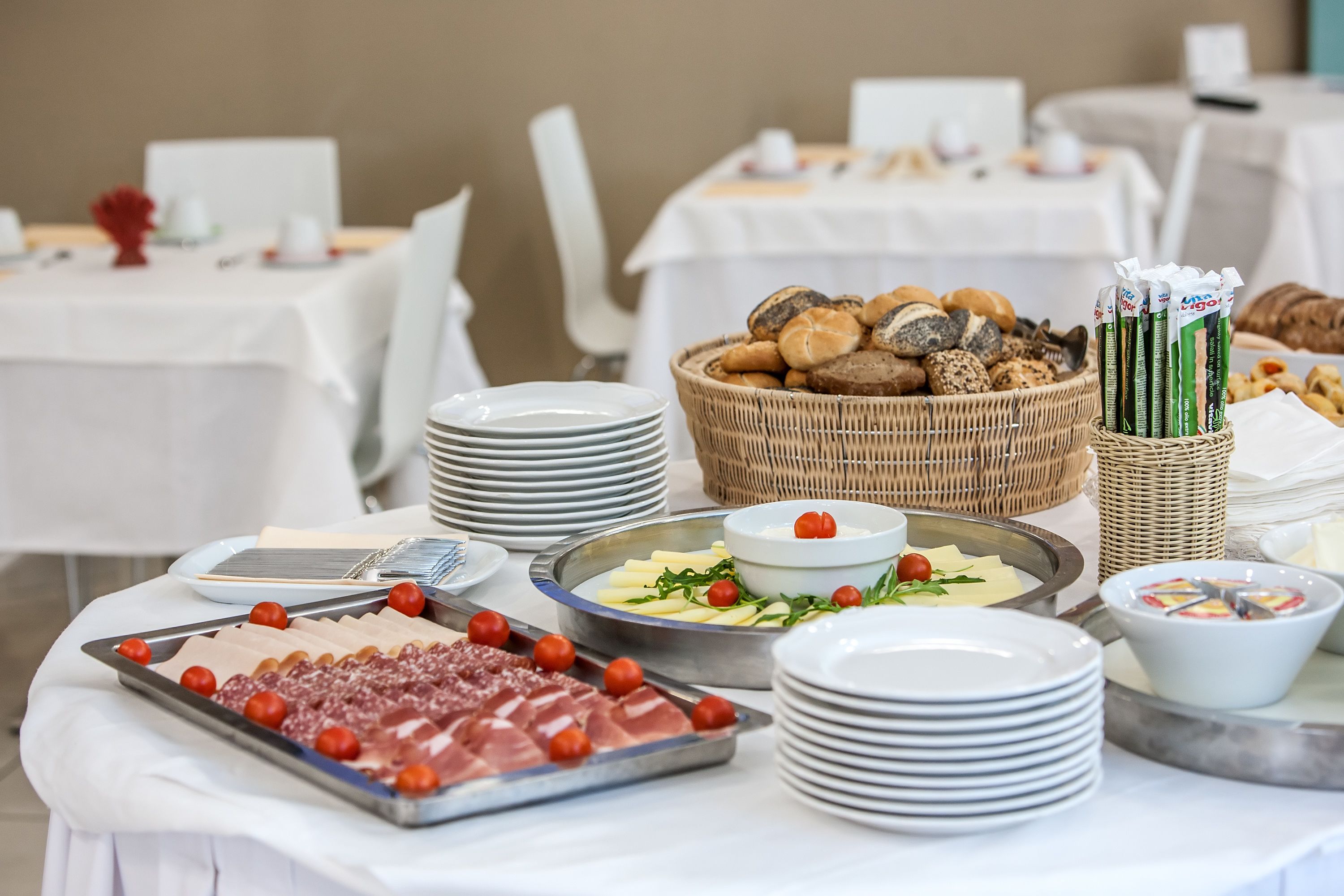 Un tavolo per buffet con diversi cibi, tra cui carni, formaggi e pane, disposti su tovaglie bianche.