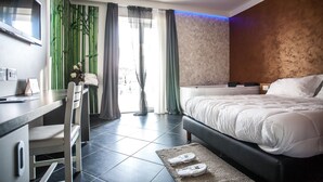 Habitación de hotel con cama, escritorio y silla. Se aprecia una ventana con cortinas, una pared con diseño texturizado y una alfombra pequeña en el suelo.