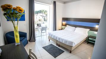 Habitación de hotel con cama, escritorio, silla, un jarrón con flores y vistas al exterior.