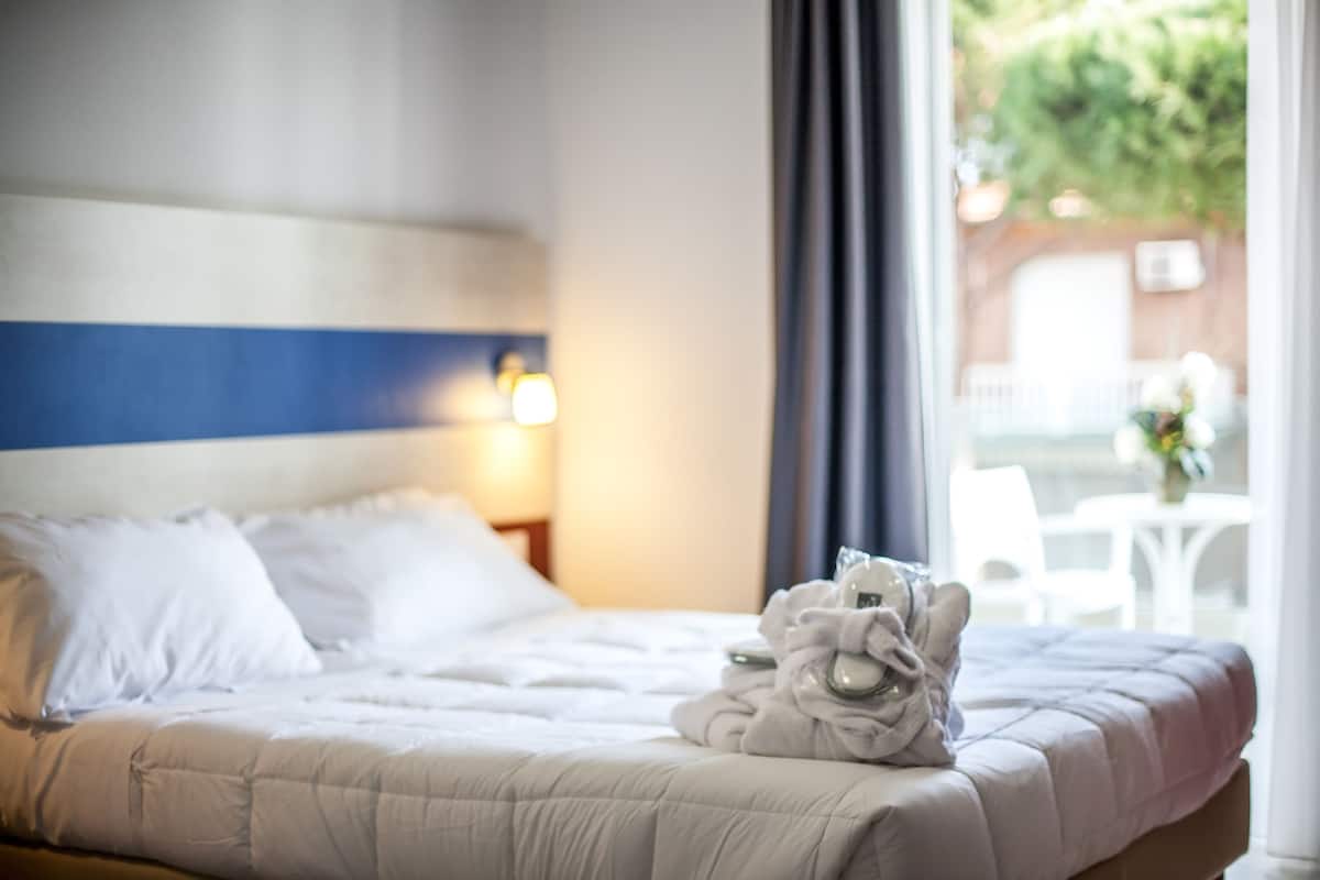 A neatly made bed with white bedding and a towel stack on the side.