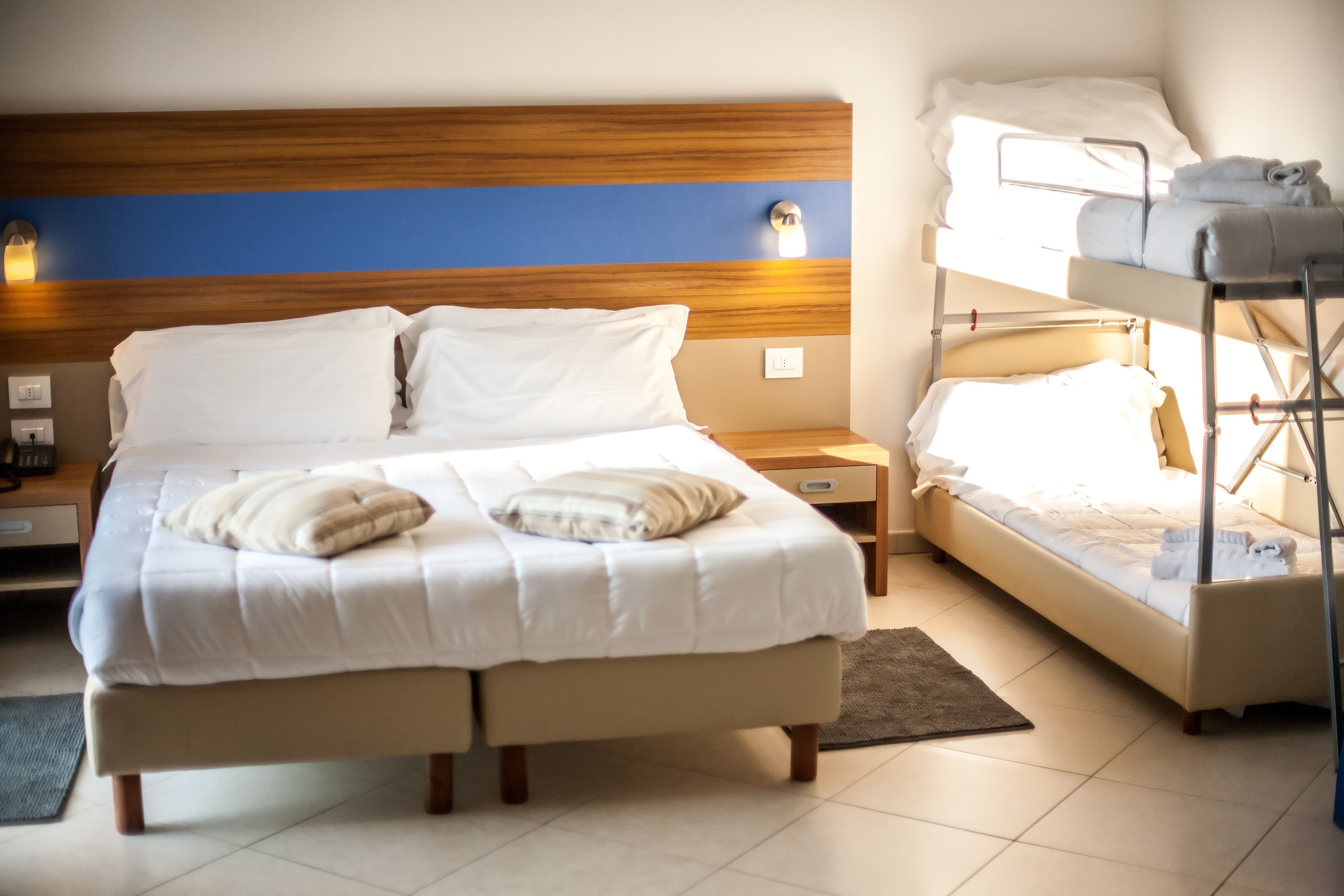 A double bed with a wooden headboard, a bedside table with a lamp, and a bunk bed with towels.