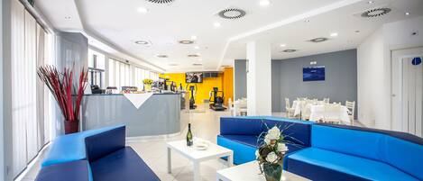 A modern hotel lobby with blue seating, a reception desk, and a dining area.