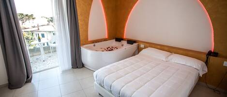 A bedroom with a large bed, a bathtub, and a view of the outside.