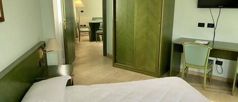 A hotel room with a bed, a desk, a chair, a television, and a wardrobe.
