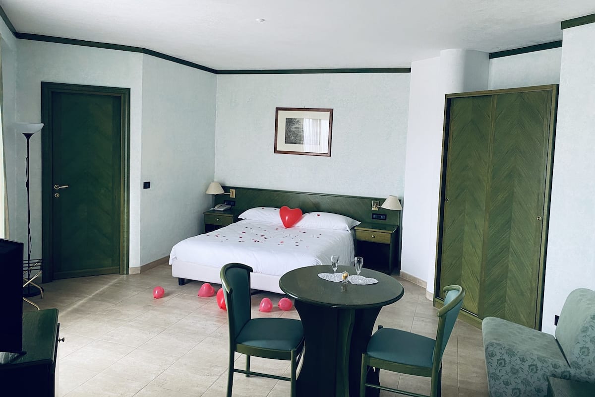 Quarto de hotel com cama, mesas de cabeceira, escrivaninha e uma cadeira.