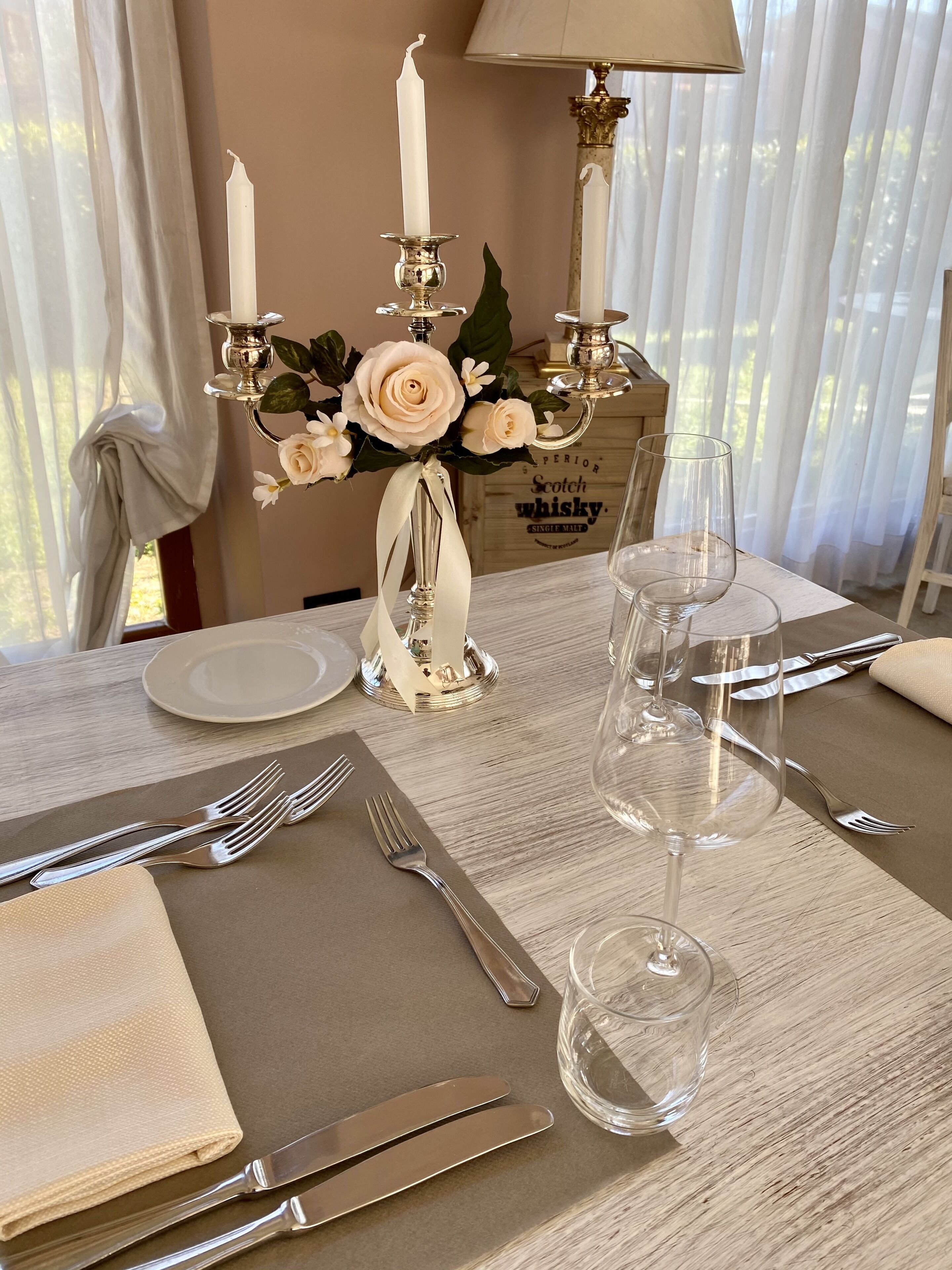 Una mesa de comedor dispuesta con un florero, velas y copas de vino vacías.