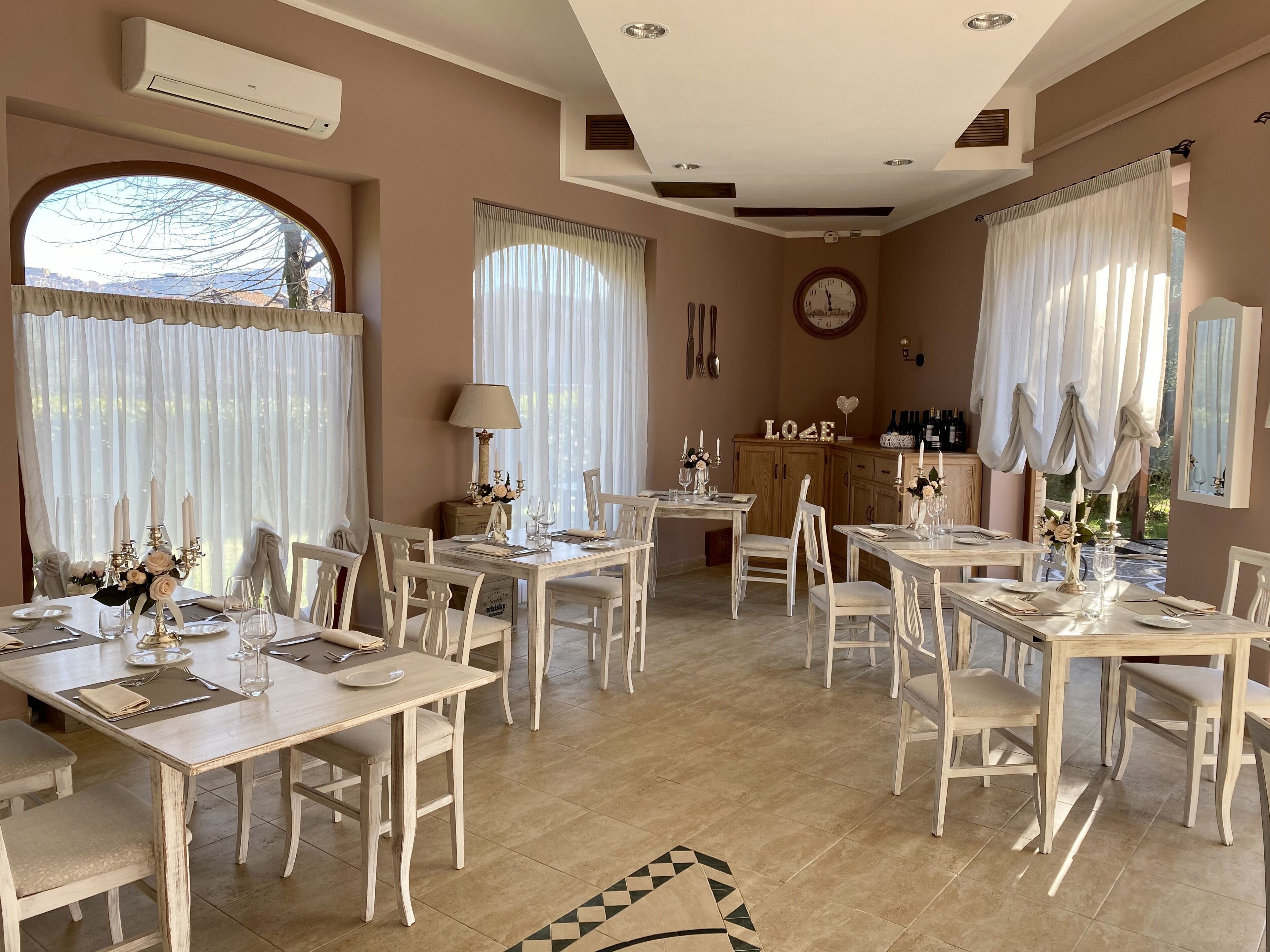 A dining area with multiple tables and chairs, a clock on the wall, and a cabinet with bottles.