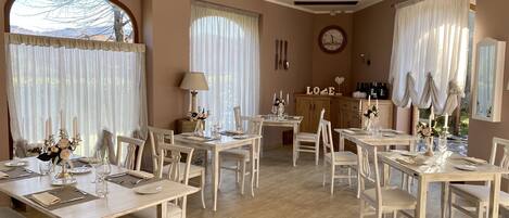 A dining area with multiple tables and chairs, a clock on the wall, and a cabinet with bottles.