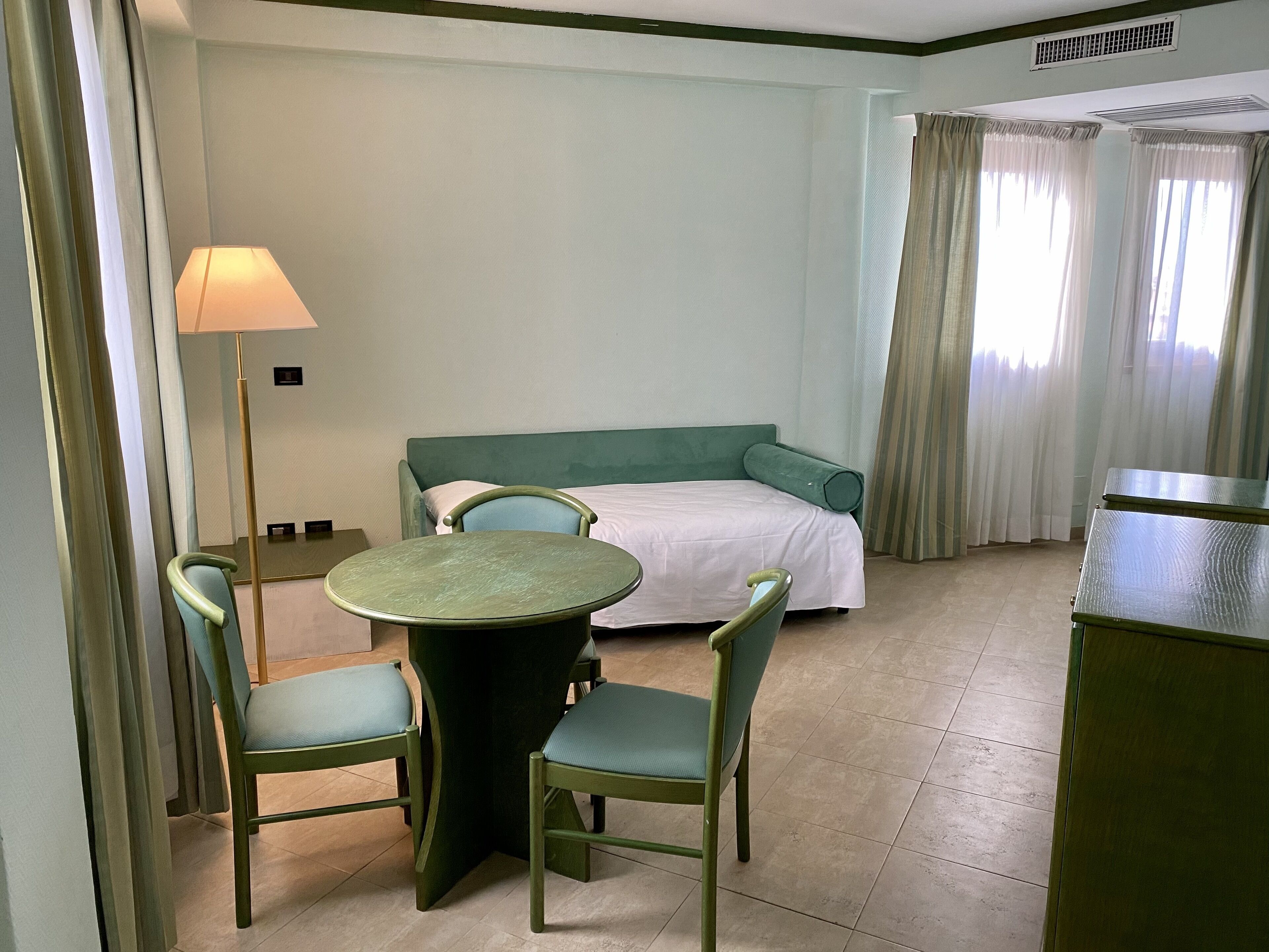 A hotel room with a bed, a table, two chairs, a lamp, and a window with curtains.