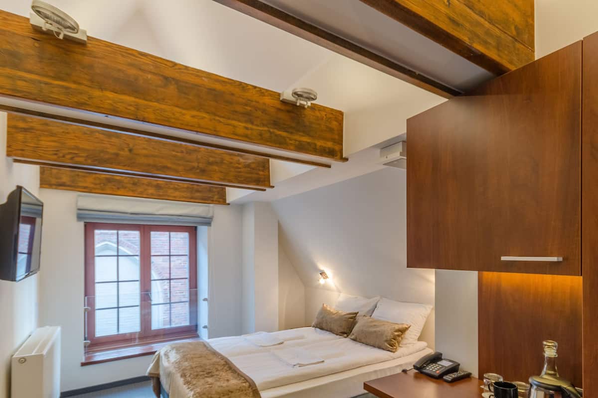 A bedroom with a bed, bedside table, lamp, and a window with a view of the outside.