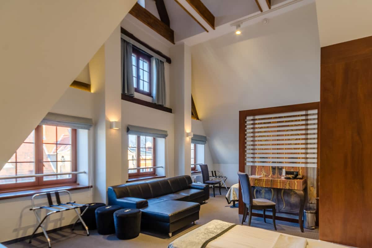 A modern loft bedroom with a sloped ceiling, large windows, a sofa, a desk, and a dining area.