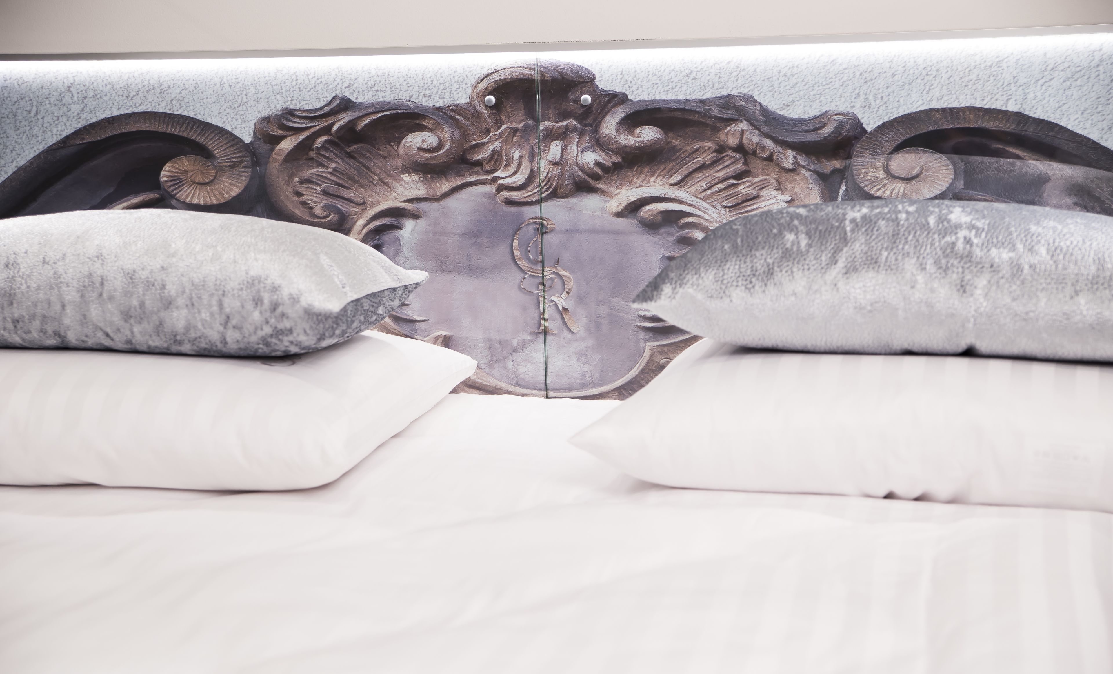 A bed with ornate headboard, white bedding, and decorative pillows.