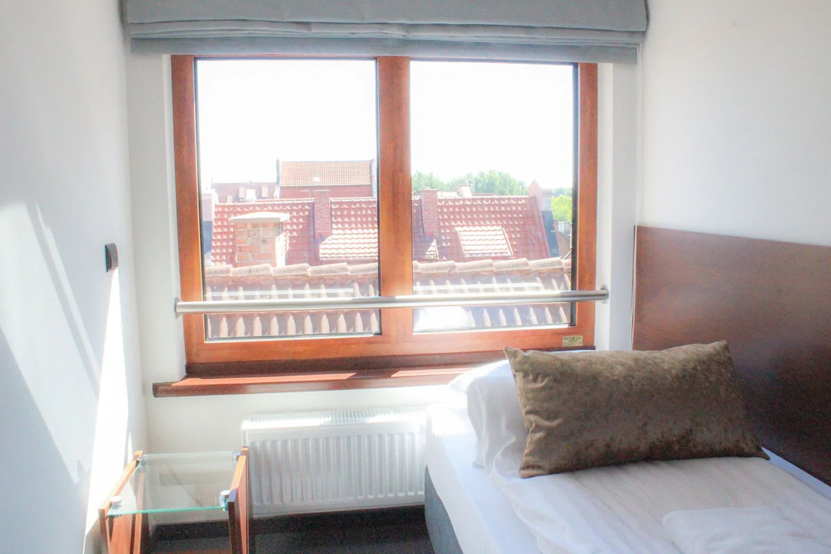 Une chambre d’hôtel avec un lit, une fenêtre donnant sur des immeubles et un radiateur situé sous la fenêtre.