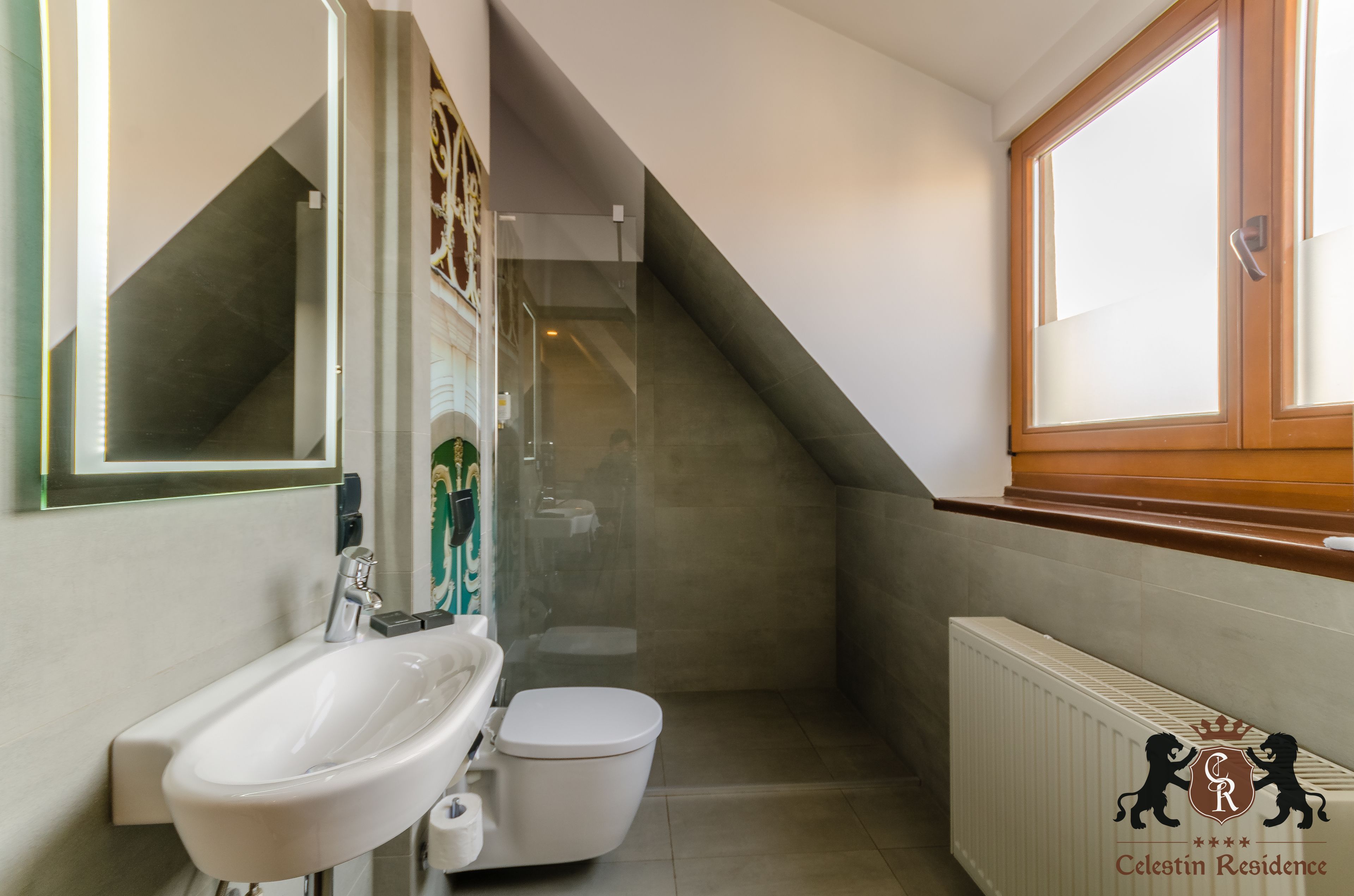 A modern bathroom with a white sink, toilet, and shower. There is a window with a wooden frame and a radiator on the wall.