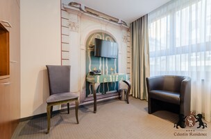 Una camera d'albergo con camino, una scrivania, due poltrone e un'ampia finestra con tende.