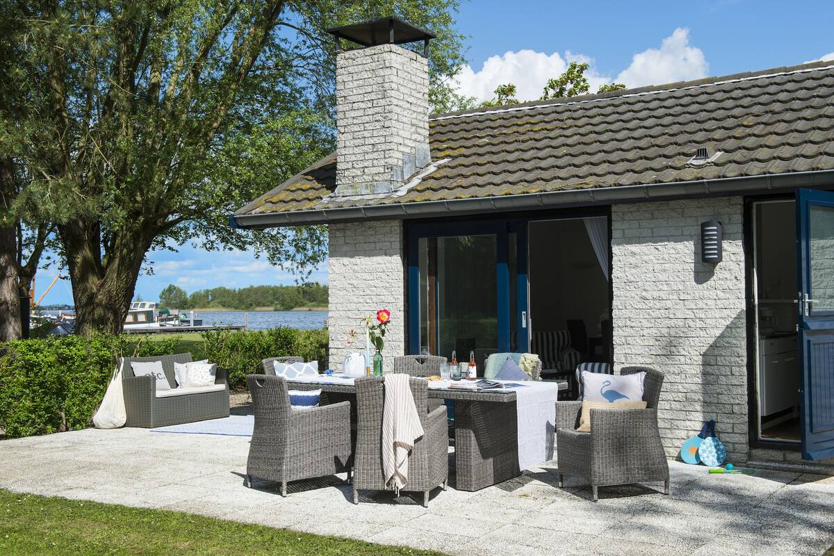 An outdoor seating area with wicker furniture, a stone chimney, and a view of the lake.