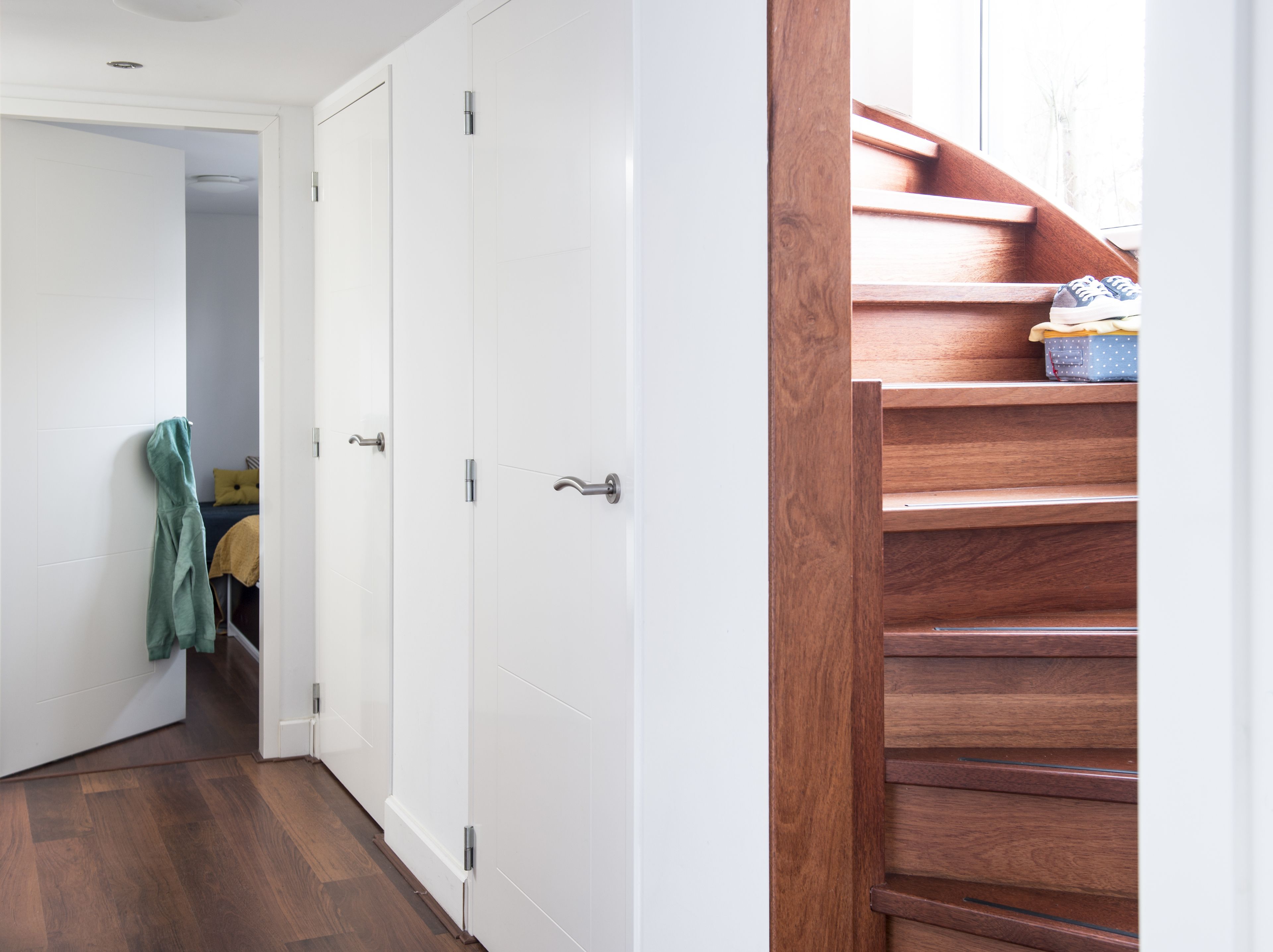 A hallway with white doors, a wooden staircase, and a glimpse of a bed with a yellow blanket.