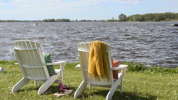 Two Adirondack chairs by a lake with a boat in the distance.