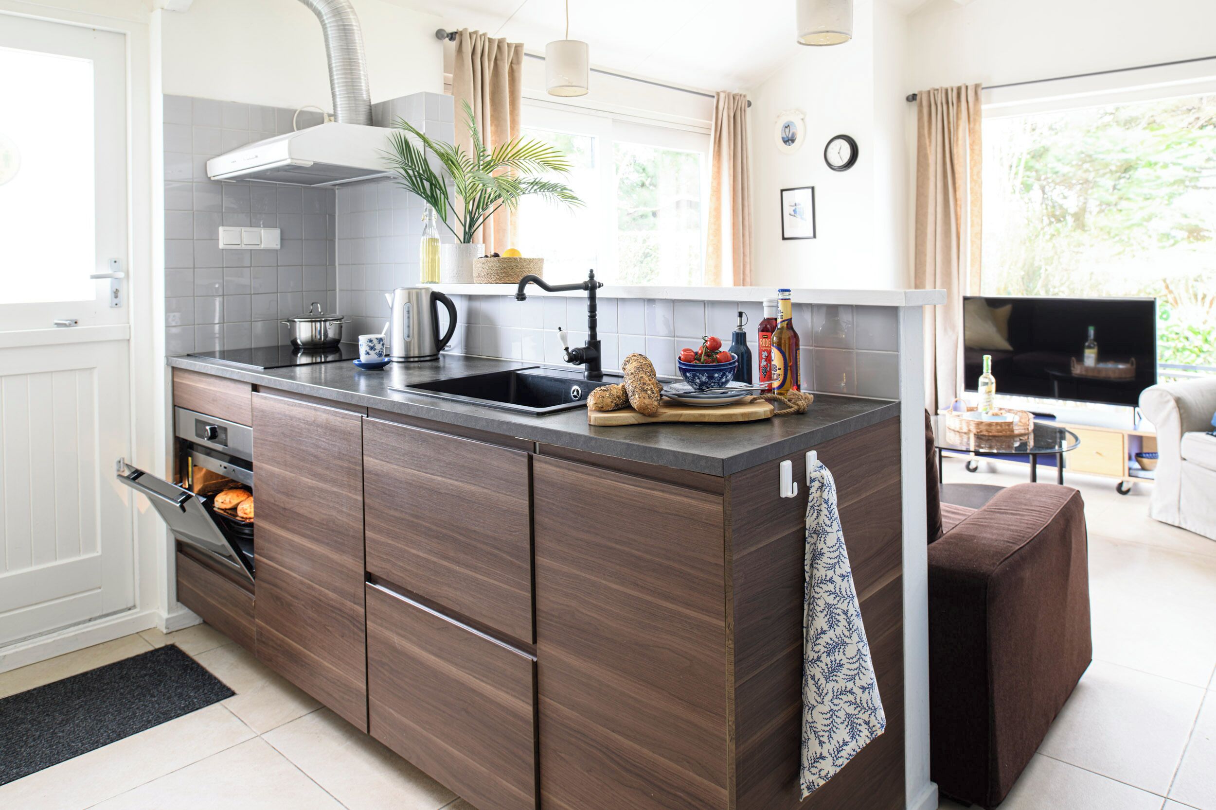 A modern kitchen with a built-in oven, a sink, and a dining area with a sofa and TV.