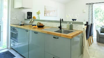 Une cuisine moderne avec un plan de travail en bois, un évier en acier inoxydable et une machine à café. Une fenêtre offre une vue sur la verdure environnante.