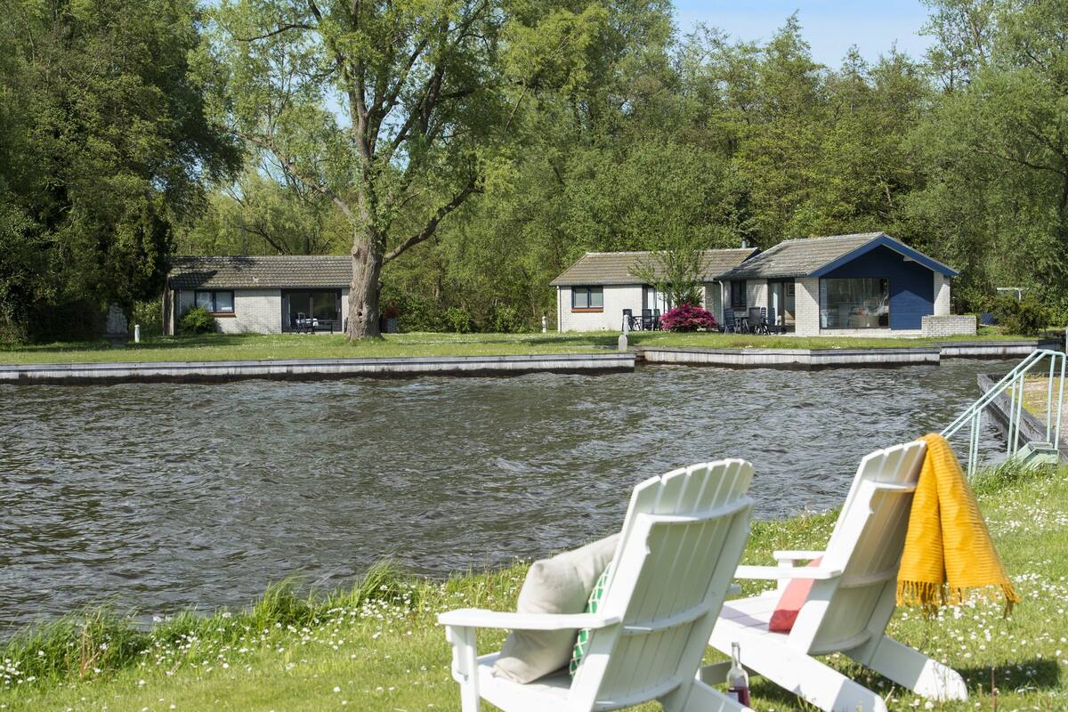 A lakeside view with two cabins, one with a blue roof and another with a grey roof, both with attached porches.