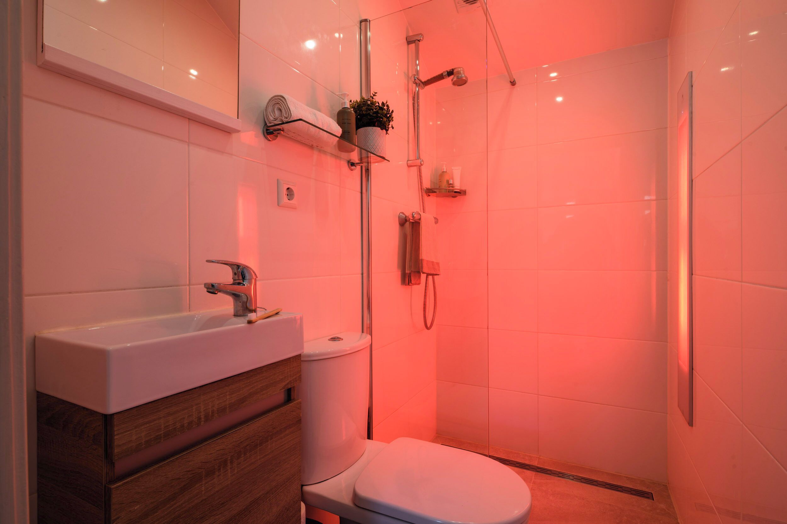 Ein modernes Badezimmer mit einem weißen Waschbecken, einem Holz-Waschtisch und einer Duschkabine aus Glas.