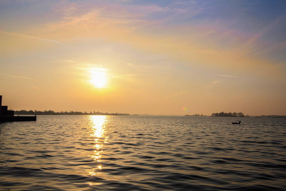A sunset over a calm body of water with a distant shoreline and a single boat.
