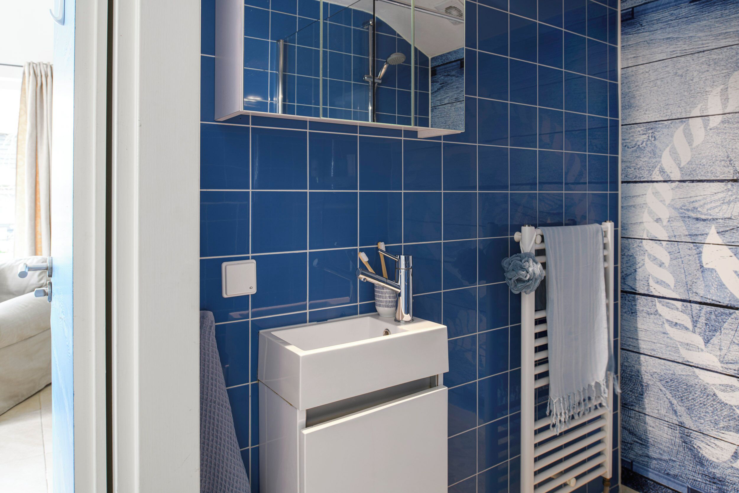 A bathroom with blue tiles, a white sink, a towel rack, and a mirror.
