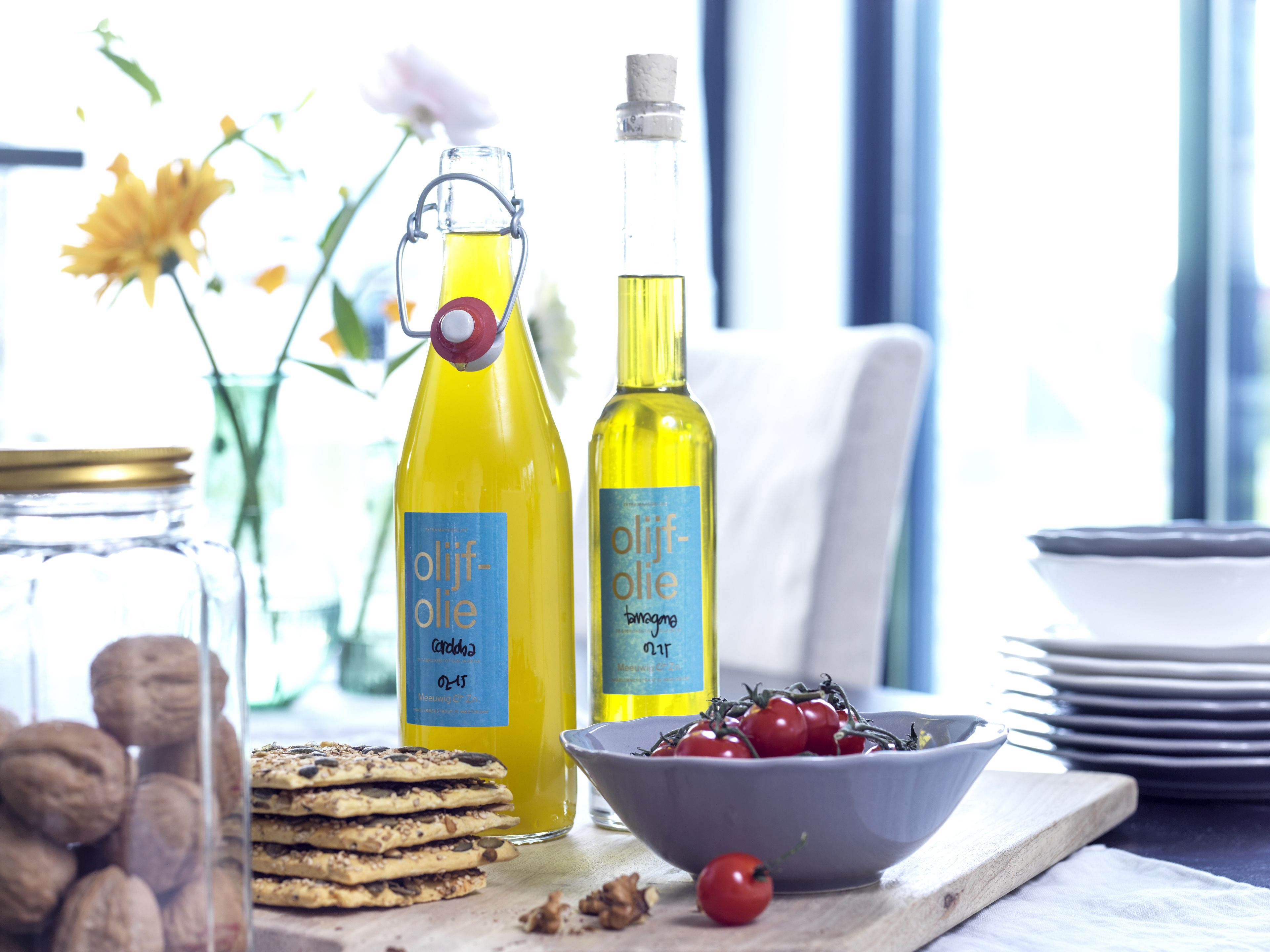 Two bottles of olive oil, a bowl of cherry tomatoes, and a stack of cookies on a wooden board.