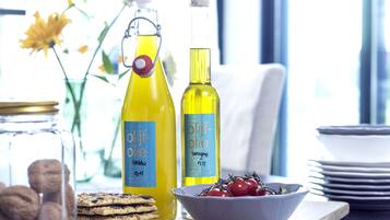 Two bottles of olive oil, a bowl of cherry tomatoes, and a stack of cookies on a wooden board.
