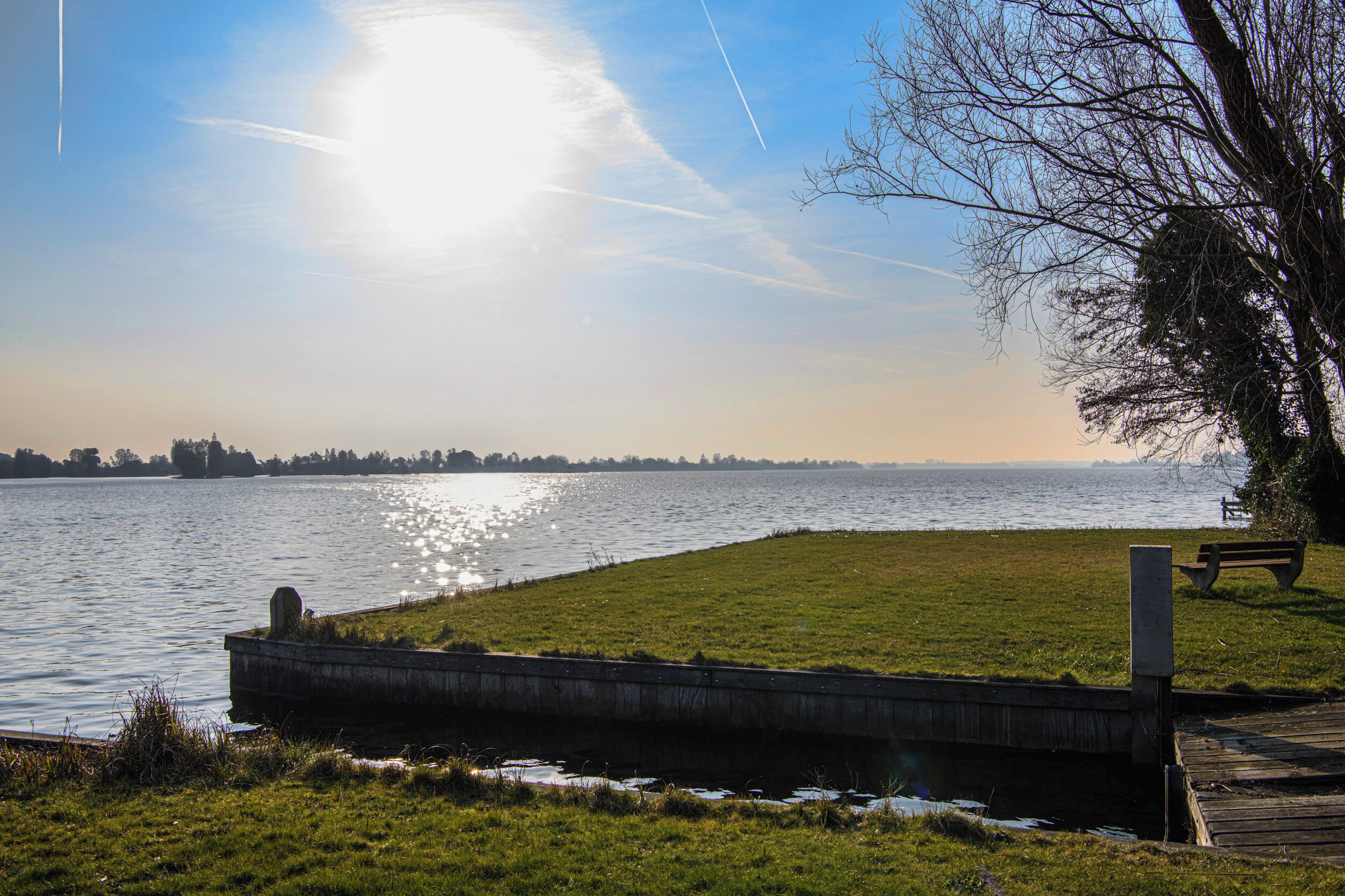 A riverside park with a grassy area, a wooden bench, and a concrete embankment.
