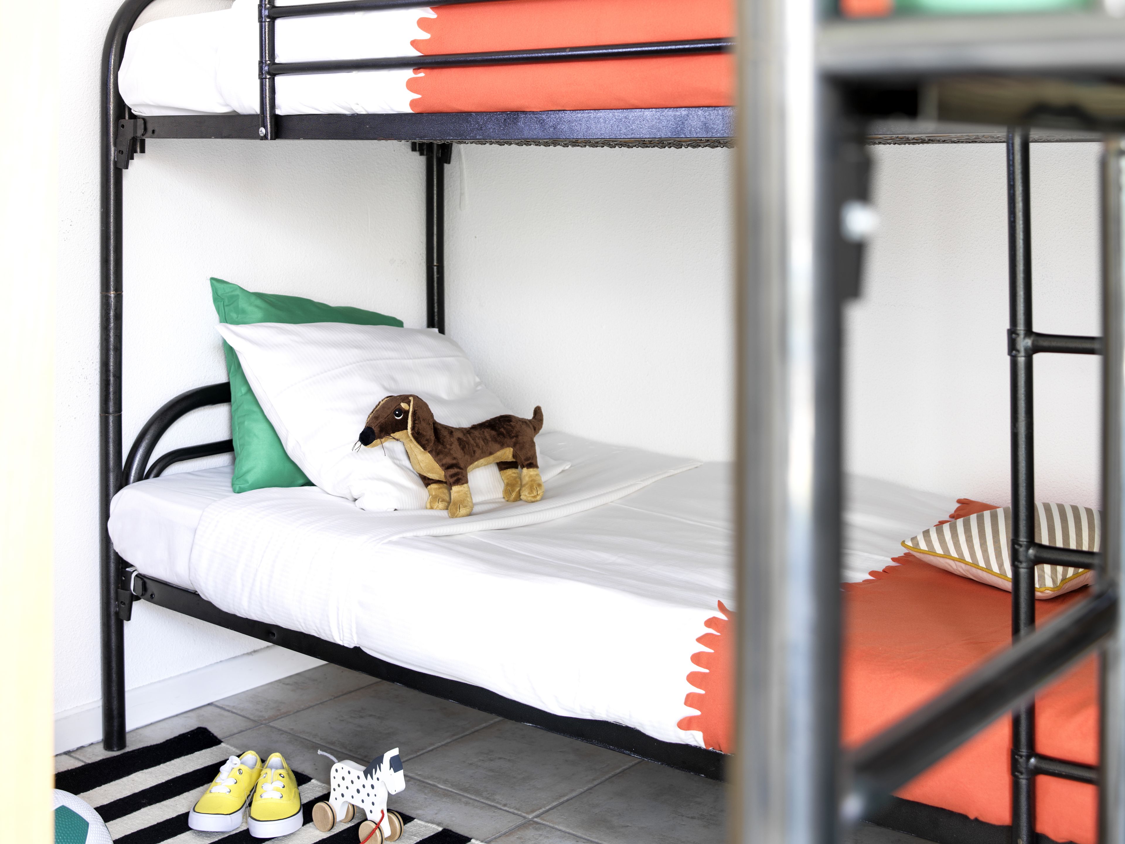 A bunk bed with a plush toy on the lower bunk, a striped rug, and a pair of yellow shoes on the floor.