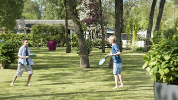 Two people playing with frisbees in a grassy park area with trees and a building in the background.