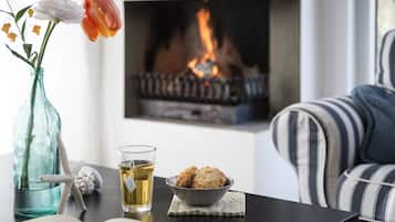 Una sala de estar con chimenea, un sofá a rayas, una mesa de vidrio con un tazón de galletas, un florero con flores y una decoración con estrella de mar.