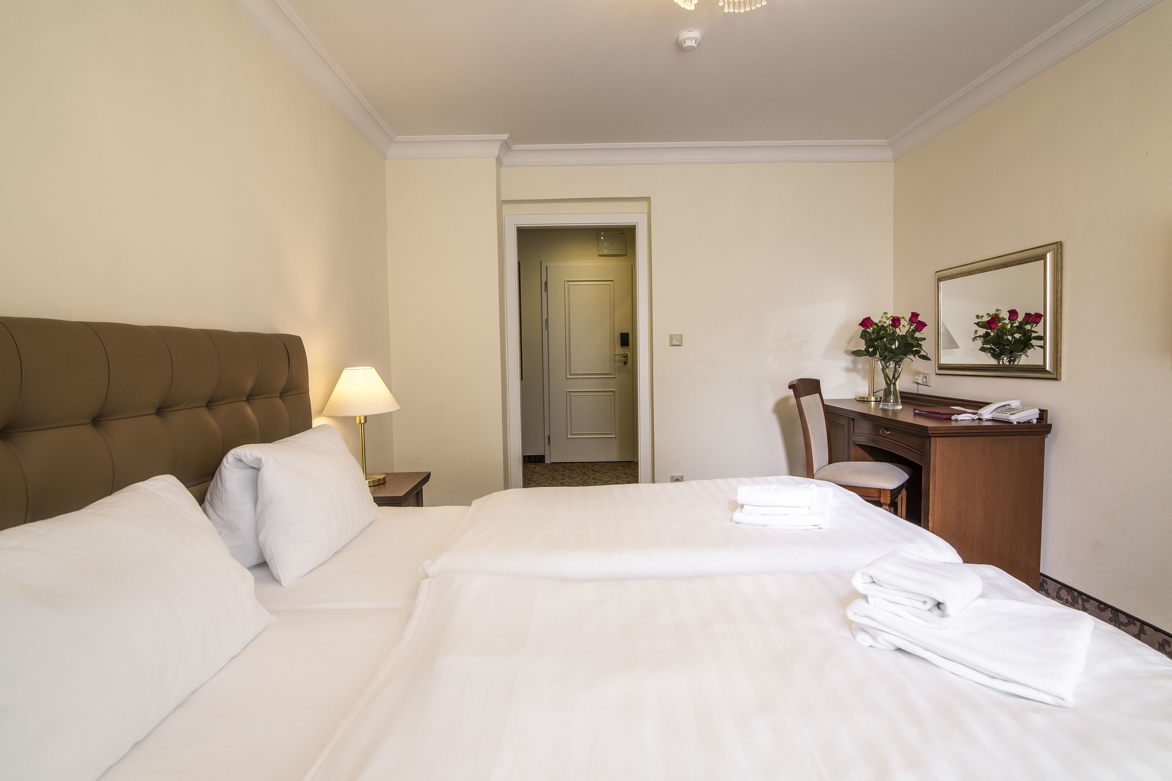 Habitación de hotel con una cama grande, un escritorio con silla, una lámpara y un espejo.