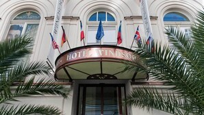 Hotel Windsorin sisäänkäynti, jossa on tyylikäs kaareva julkisivu, useita lippuja ja etualalla palmuja.
