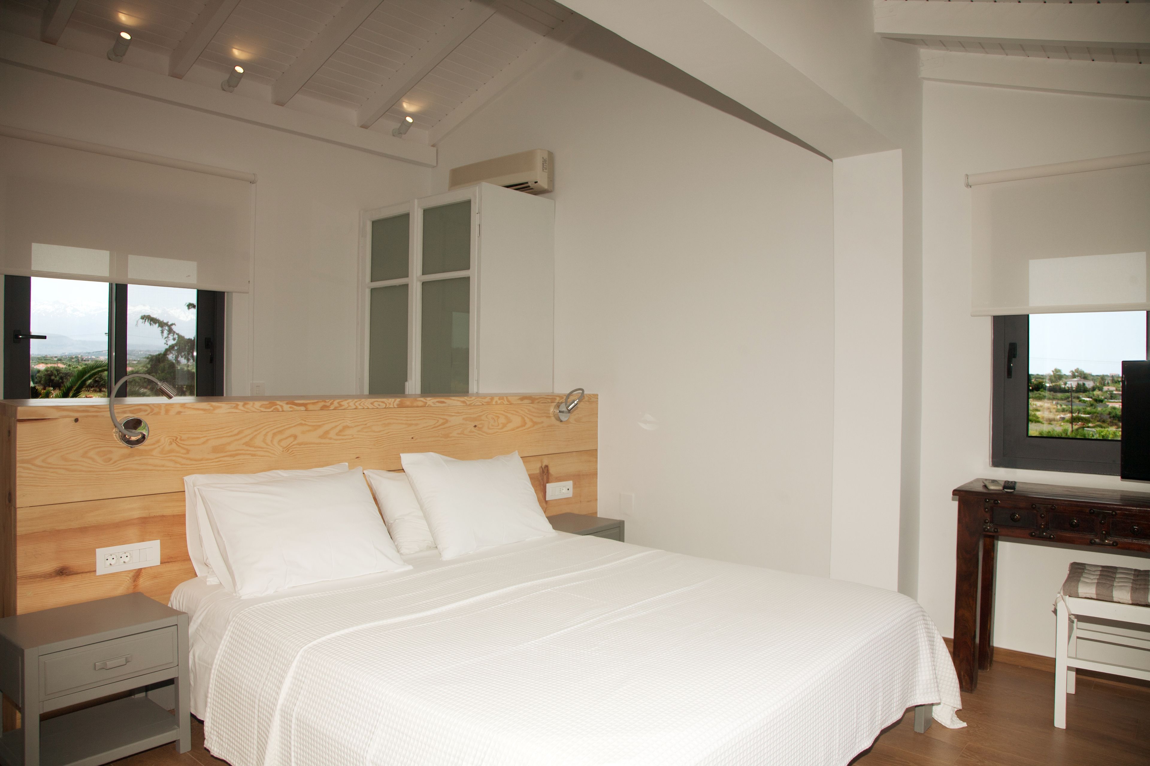A bedroom with a wooden headboard, a bed with white bedding, a nightstand, a small table, and a TV on a stand.