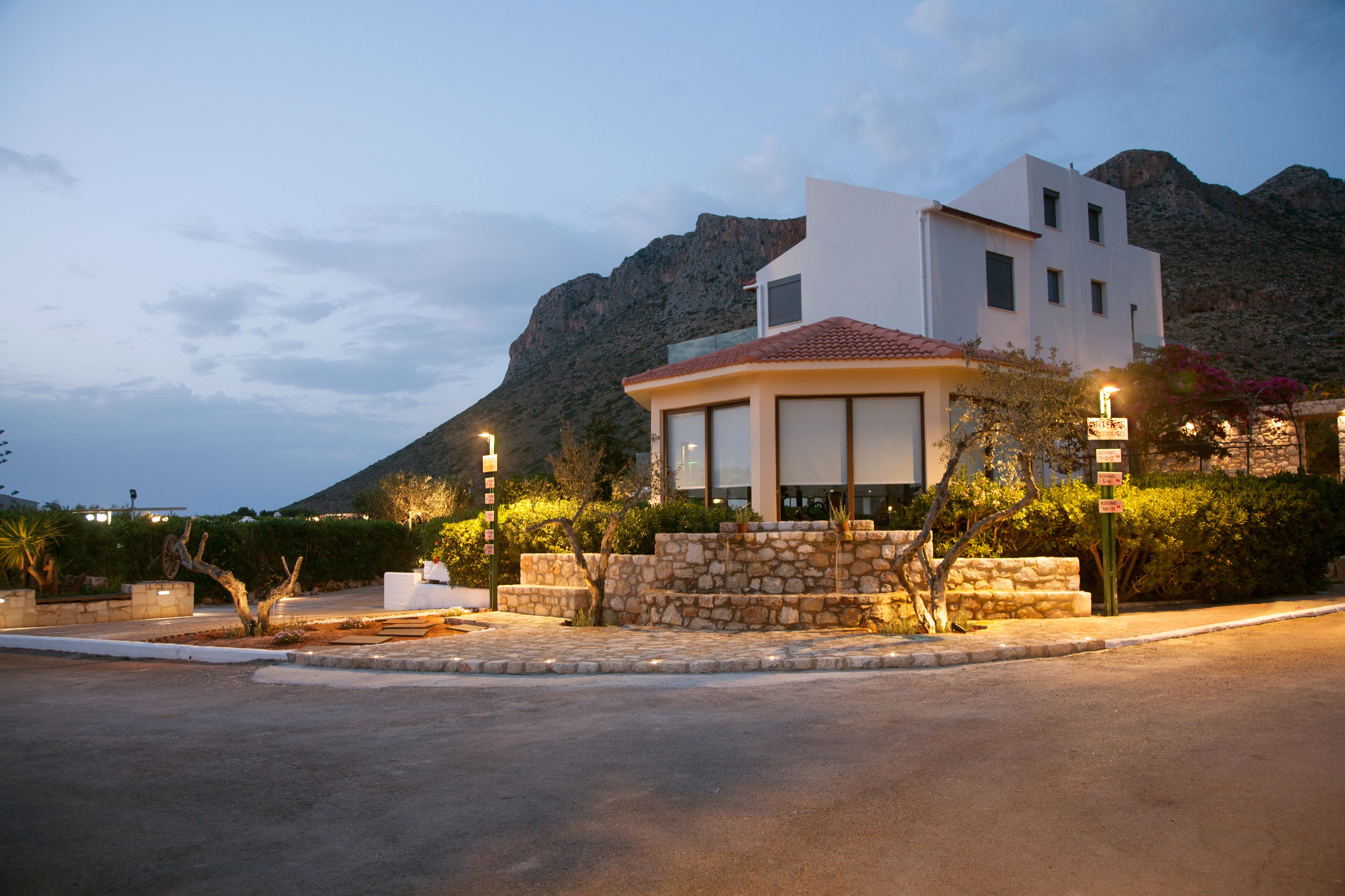 A modern building with a stone base and a white upper section, surrounded by greenery and a mountain backdrop.