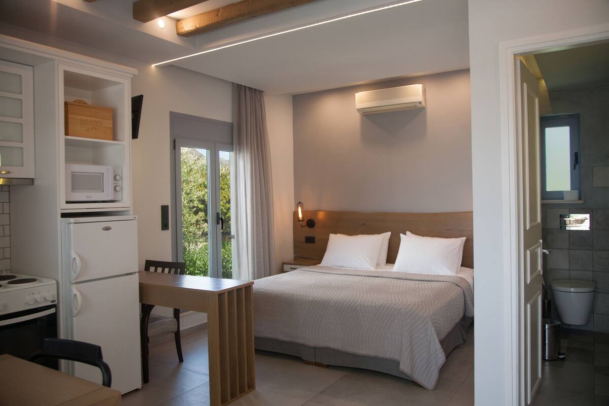 A modern hotel room with a bed, a dining area, a kitchenette, and a bathroom.