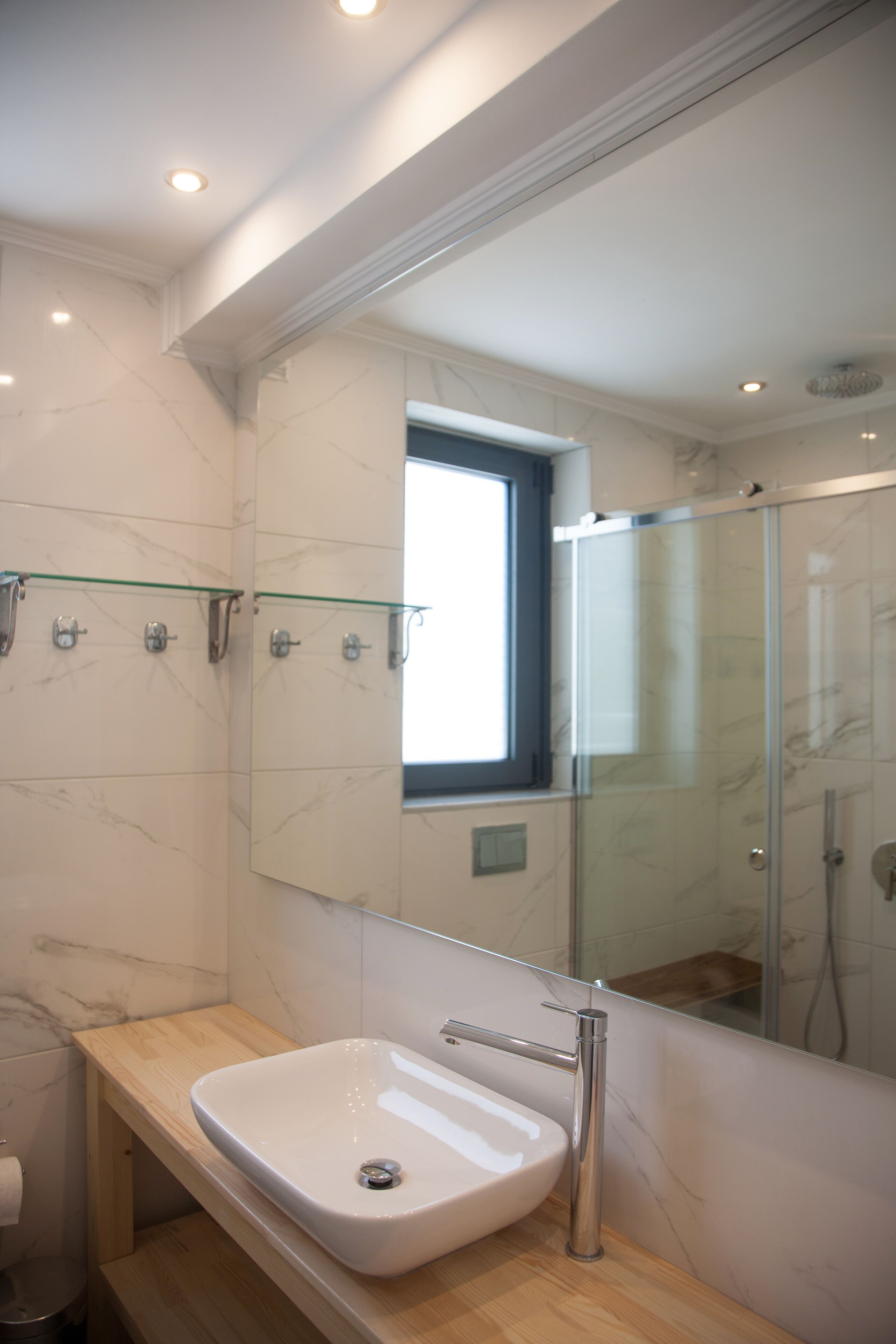 A modern bathroom with a large mirror, a glass shower enclosure, and a marble-tiled wall.