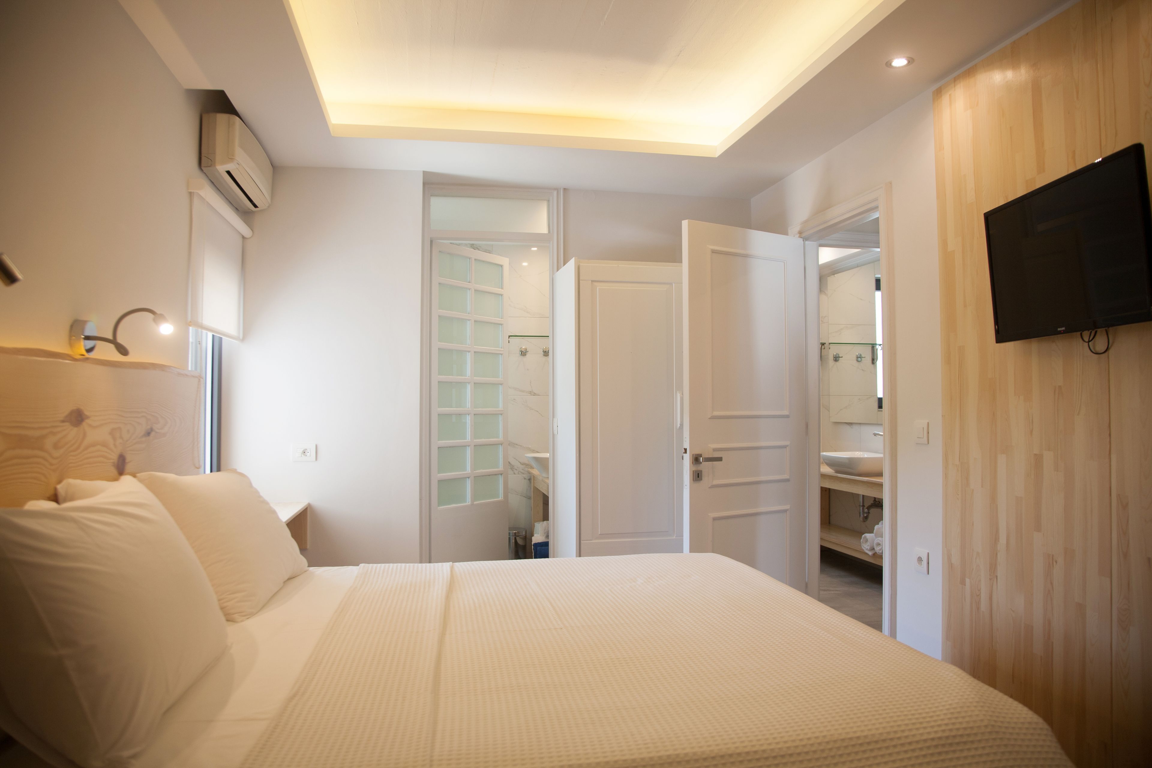 A bedroom with a bed, a TV mounted on the wall, and an open door leading to a bathroom.