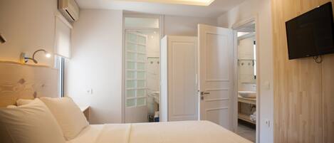 A bedroom with a bed, a TV mounted on the wall, and an open door leading to a bathroom.