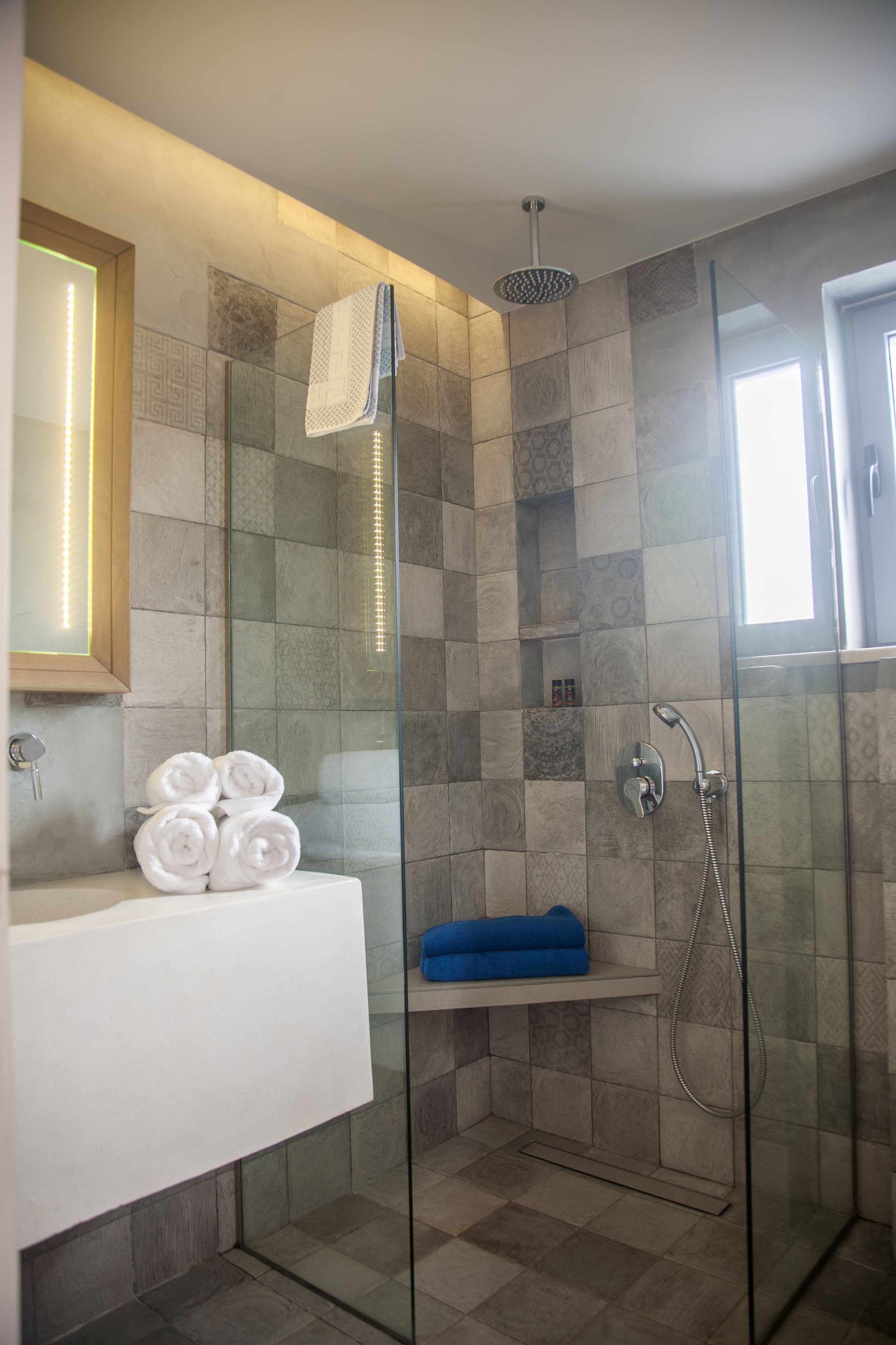 Un baño moderno con ducha acristalada, lavamanos blanco y toallas ordenadamente dobladas.