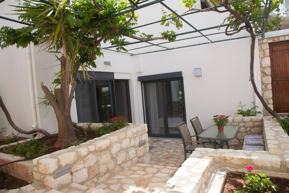 A stone-walled patio with a table and chairs, a potted plant, and a tree.