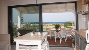 Uma zona de refeições com mesa e cadeiras, vista para o mar e área de cozinha.