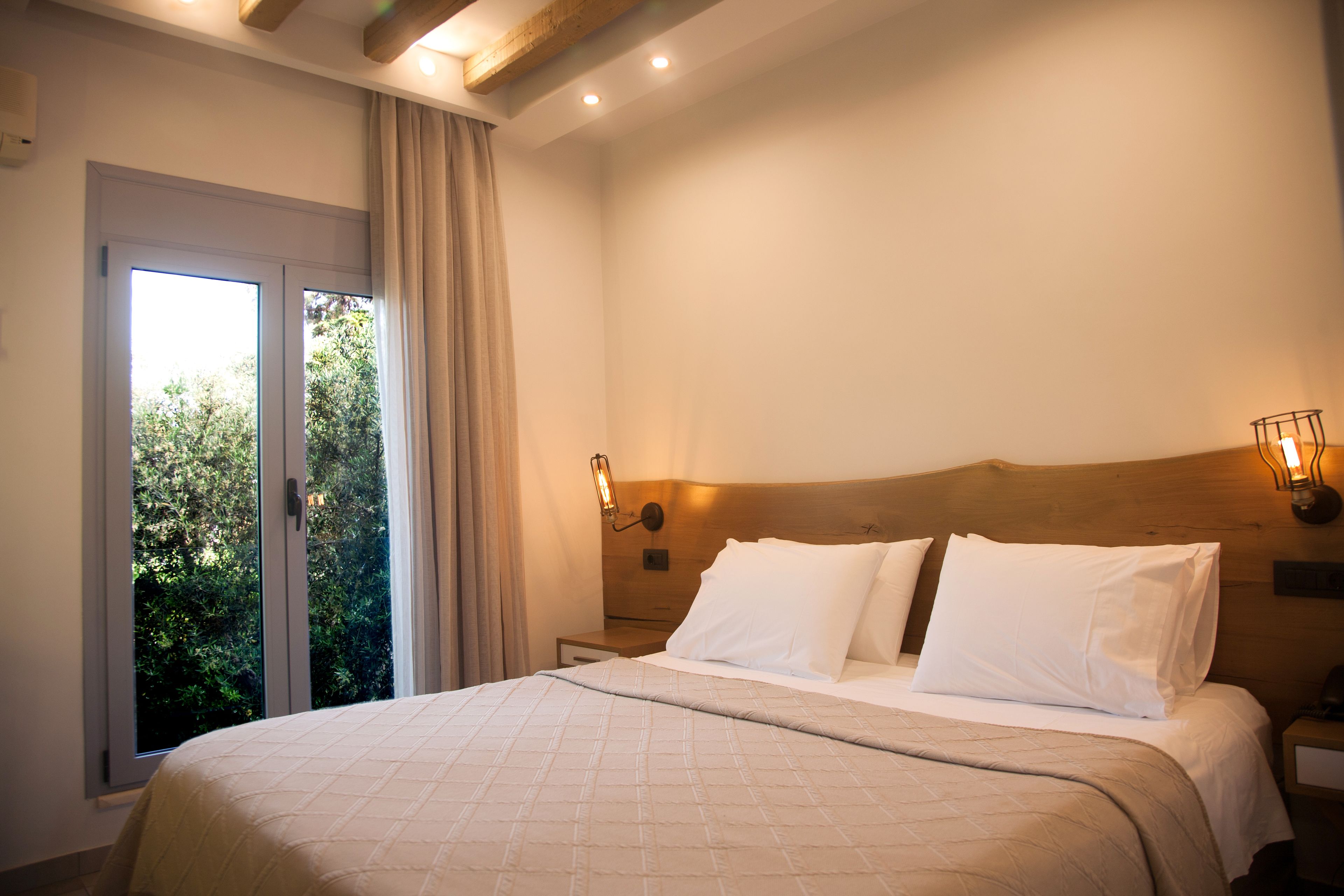 A hotel room with a large bed, a nightstand, a wall-mounted lamp, and a window with curtains.