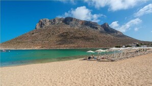 Uma praia com montanha rochosa ao fundo, água turquesa translúcida e espreguiçadeiras na orla.