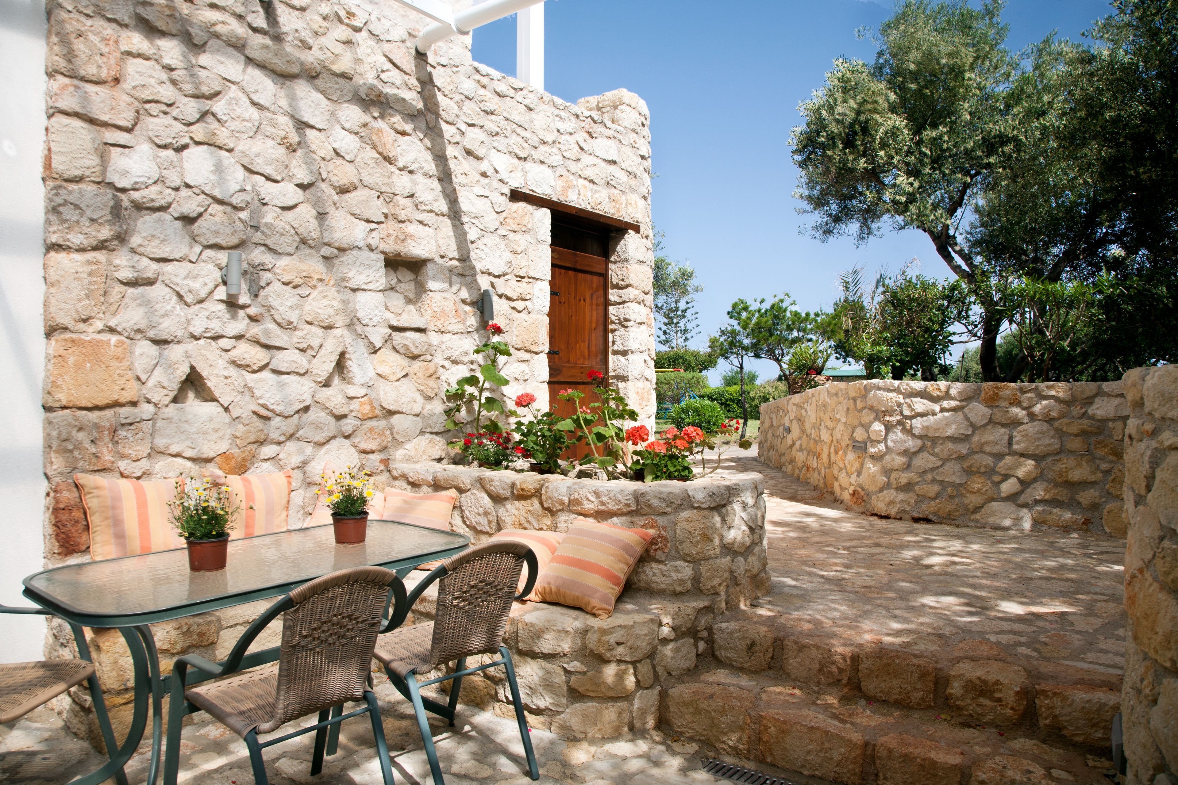 A stone building with a glass table and chairs, a wooden door, and a stone wall with steps.